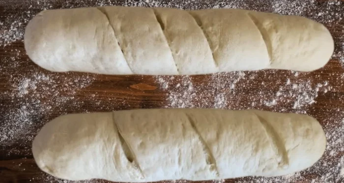 Shaped French Bread Loaves with Scored Tops on a Floured Wooden Surface