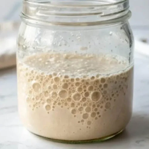 A close-up of a bubbling flour and water yeast starter in a glass jar